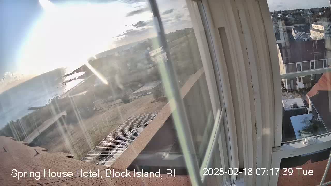 A view from a window shows a partly sunny day overlooking a coastal area with buildings, some construction, and the ocean in the distance.