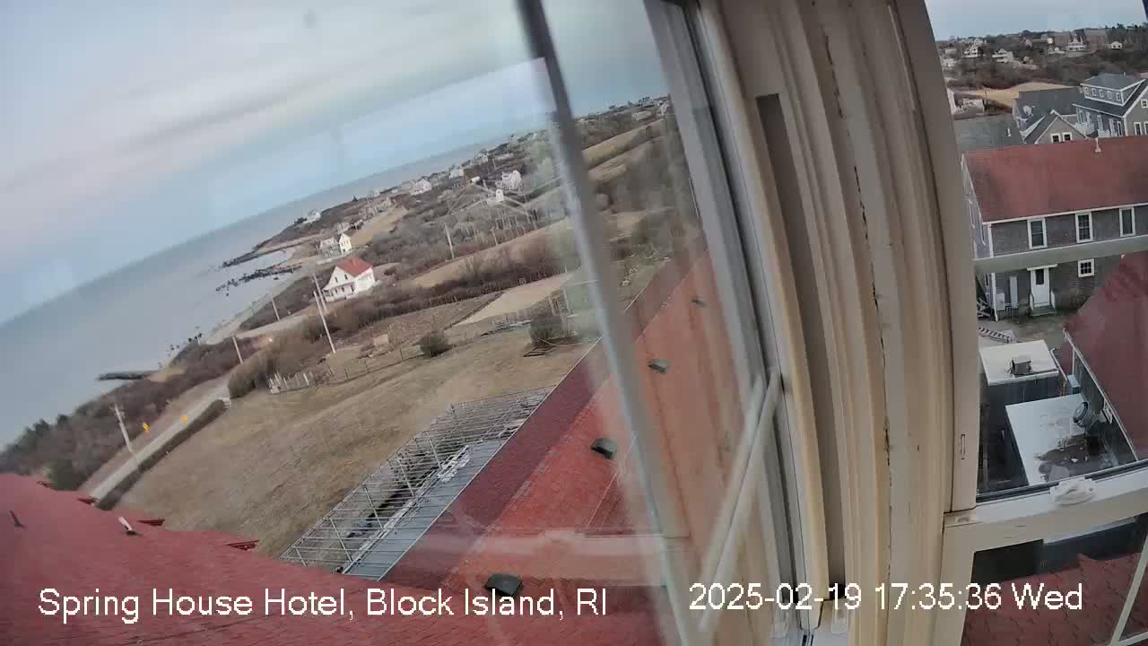 A view from a window shows a coastal town under an overcast sky, with a body of water visible in the distance.