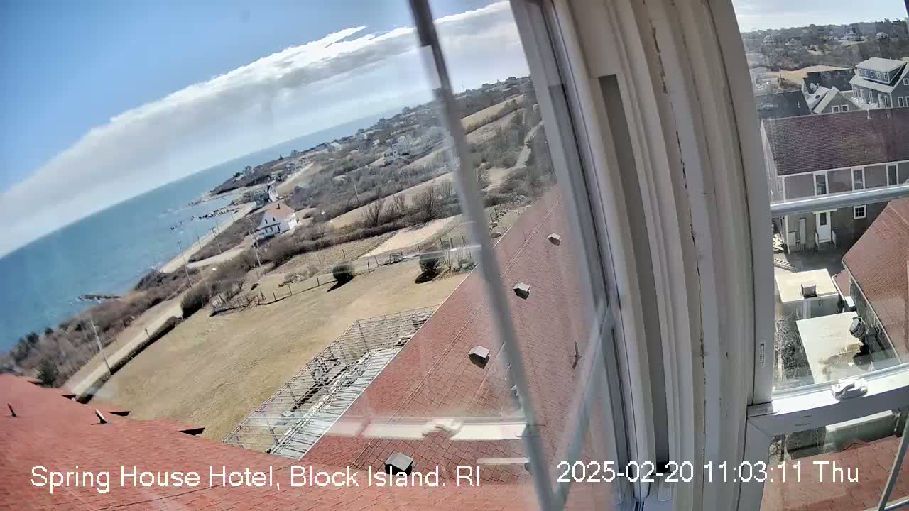A view from a window shows a partly sunny day overlooking a coastal area with buildings, open land, and the ocean.