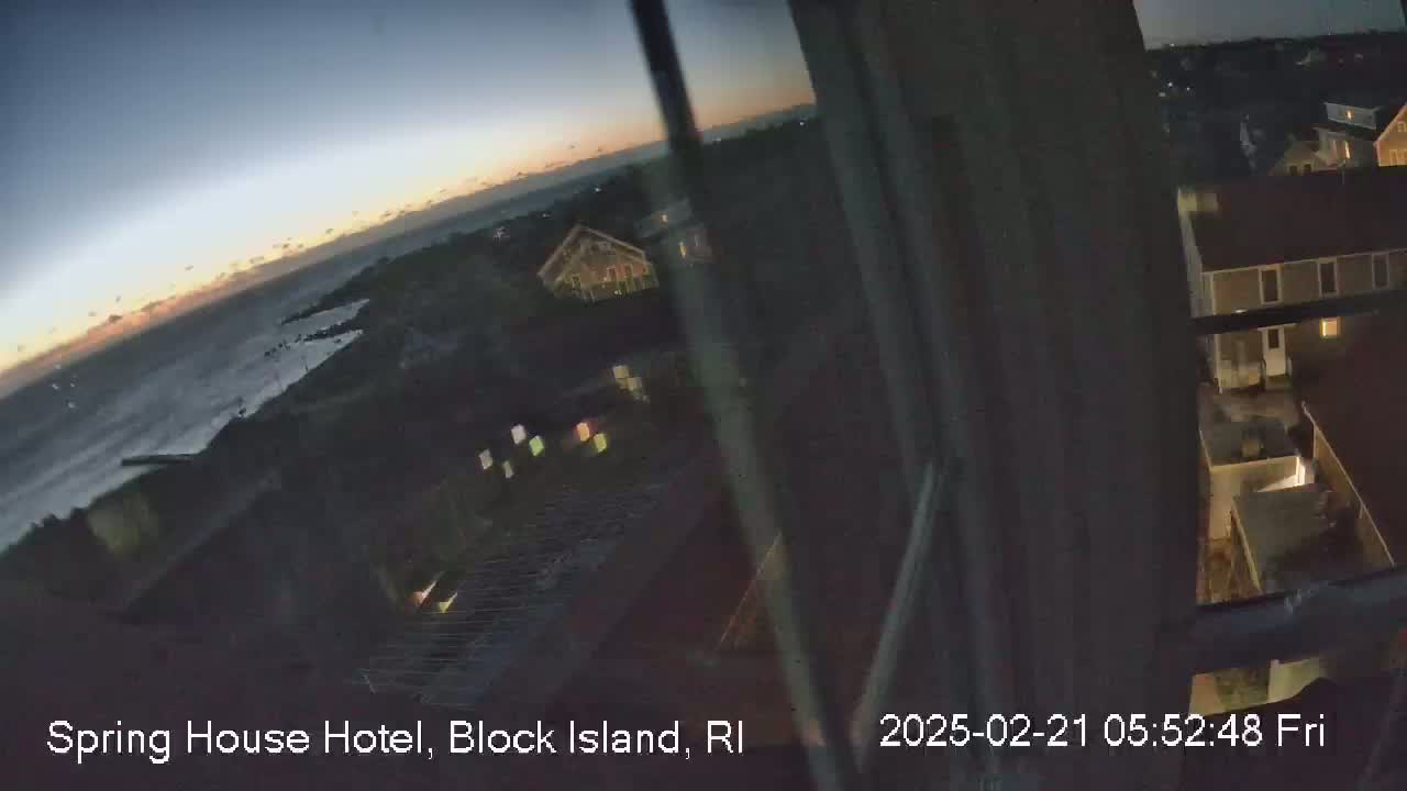 A twilight view from a window shows a dark ocean, a rocky shoreline, and dimly lit buildings.