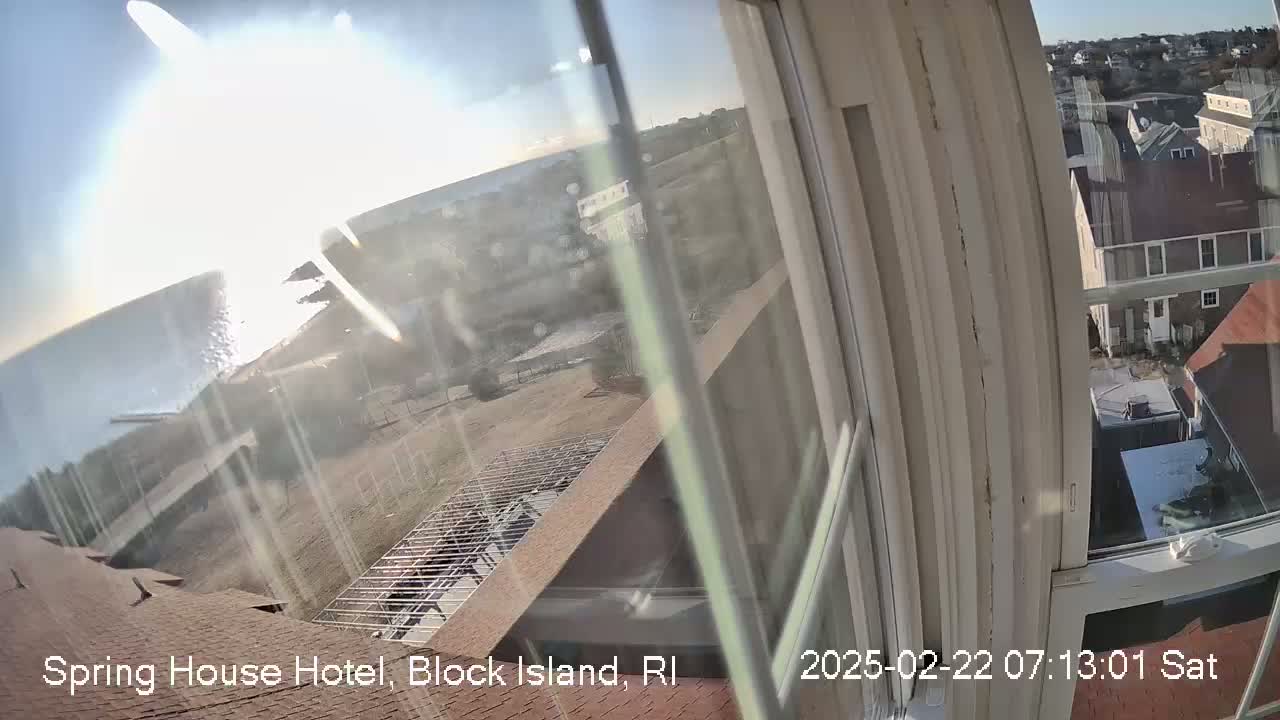 A view from a window shows a sunny day overlooking a coastline, a partially constructed structure, and other buildings, all seen through a somewhat dirty window.
