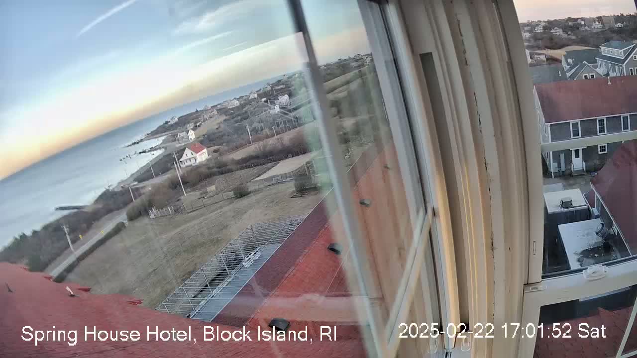 A view from a window shows a coastal town under a mostly clear sky, with a calm ocean in the distance.