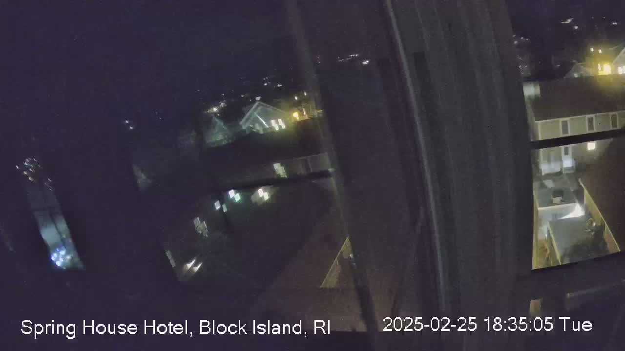 A nighttime view from a window shows a dimly lit residential area with several buildings and some scattered lights.