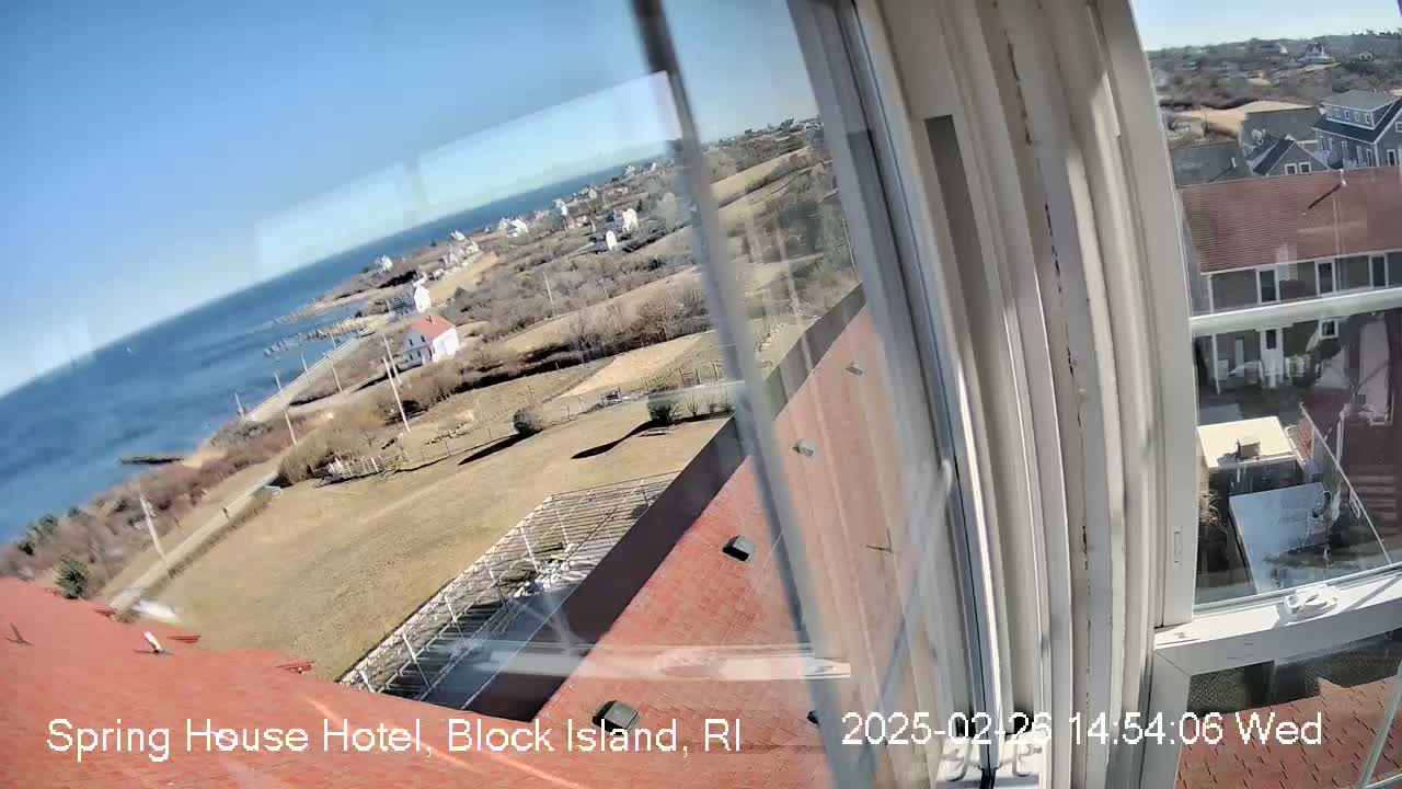 A view from a window shows a coastal scene on a sunny day, with a body of water, buildings, and land stretching into the distance.