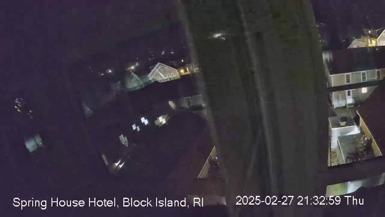 A nighttime, slightly blurry, overhead view of a residential area shows several houses and yards under a dark, possibly snowy sky.