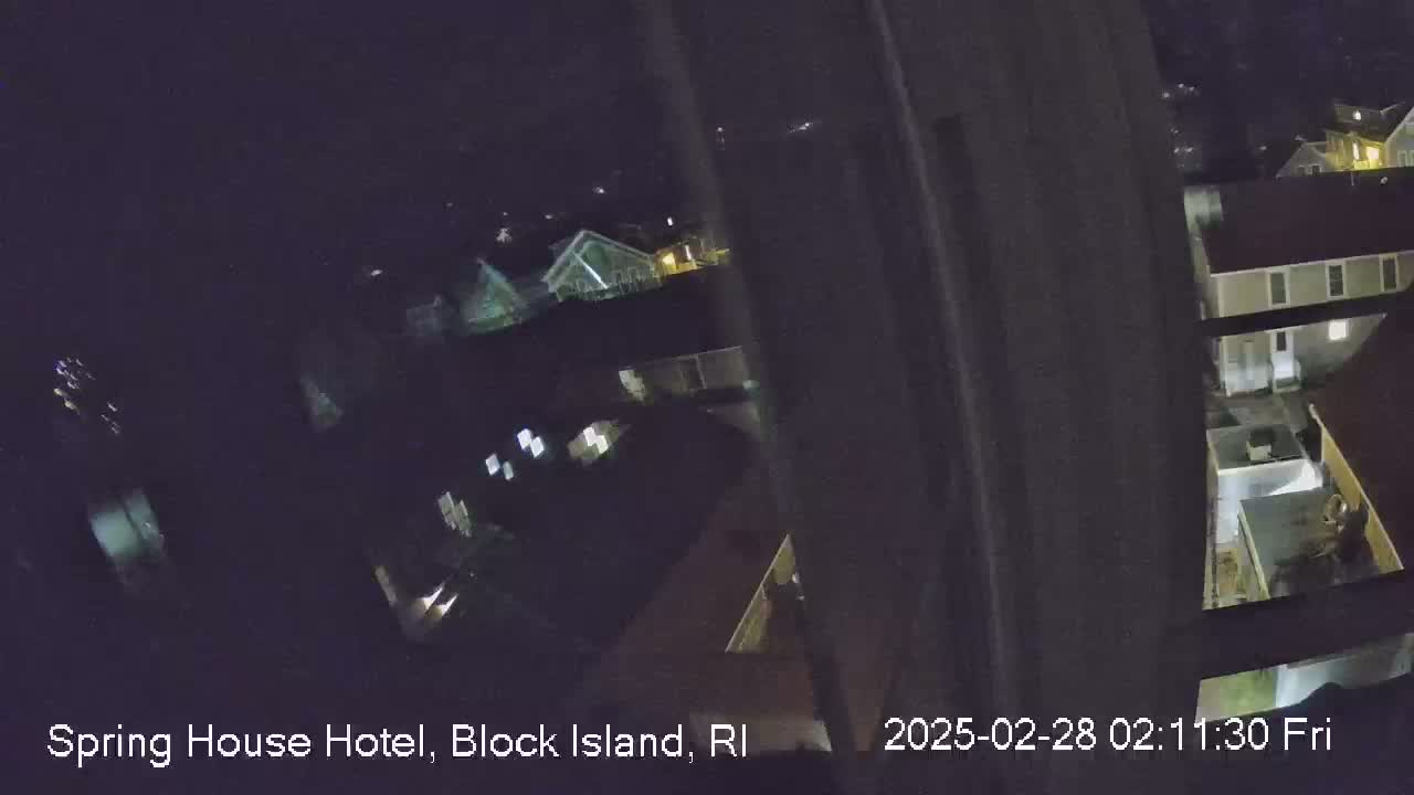 A nighttime, high-angle view shows a cluster of houses and buildings with some lights on.