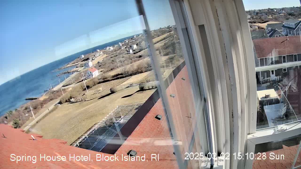 A view from a window shows a coastal town on a sunny day, with a body of water visible in the distance.