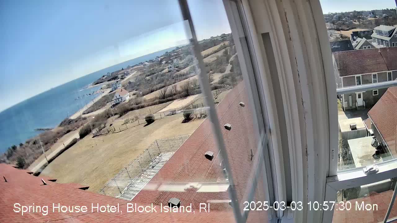 A view from a window shows a coast with a building, other structures, and open land, under sunny skies.