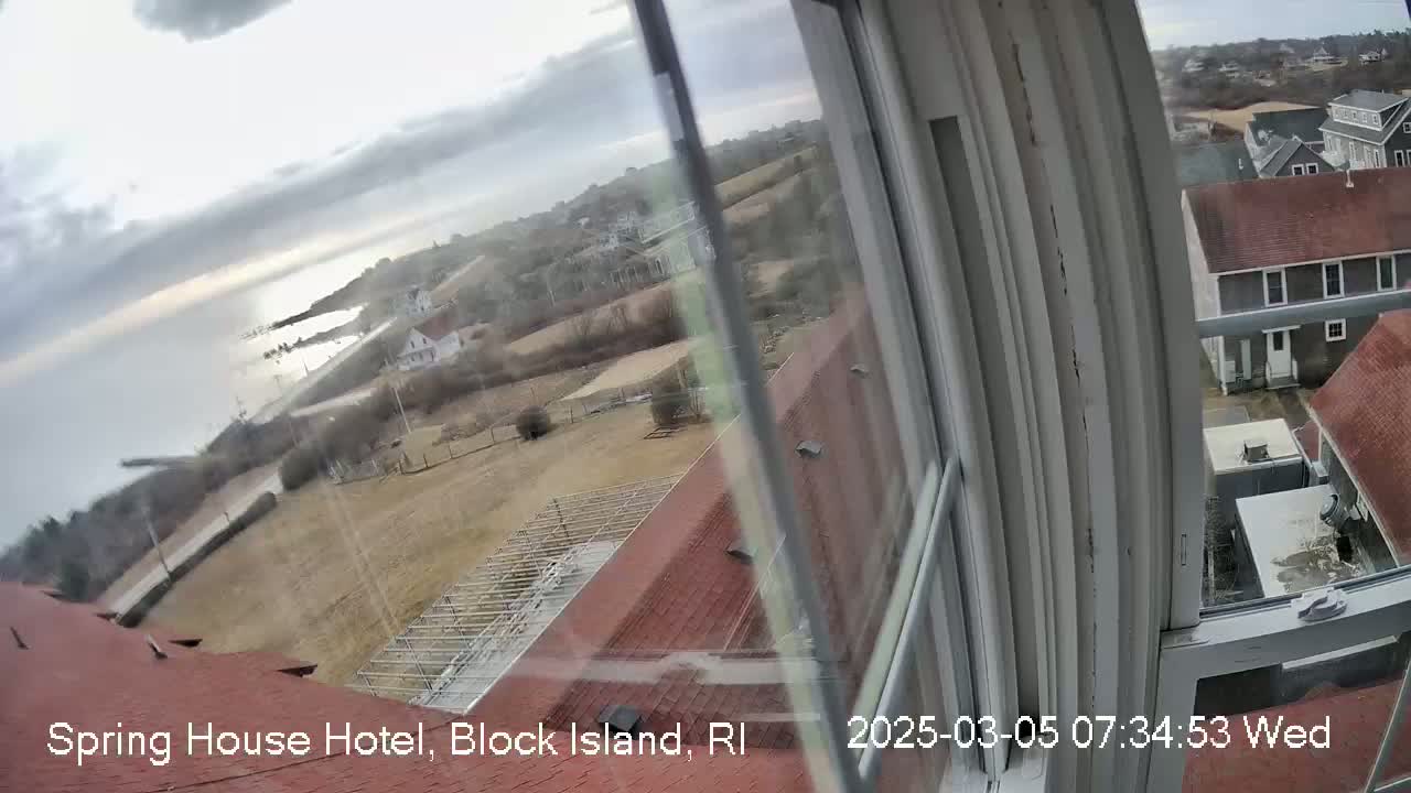 A view from a window shows a coastal scene on an overcast day, with buildings, a road, and a body of water visible in the distance.