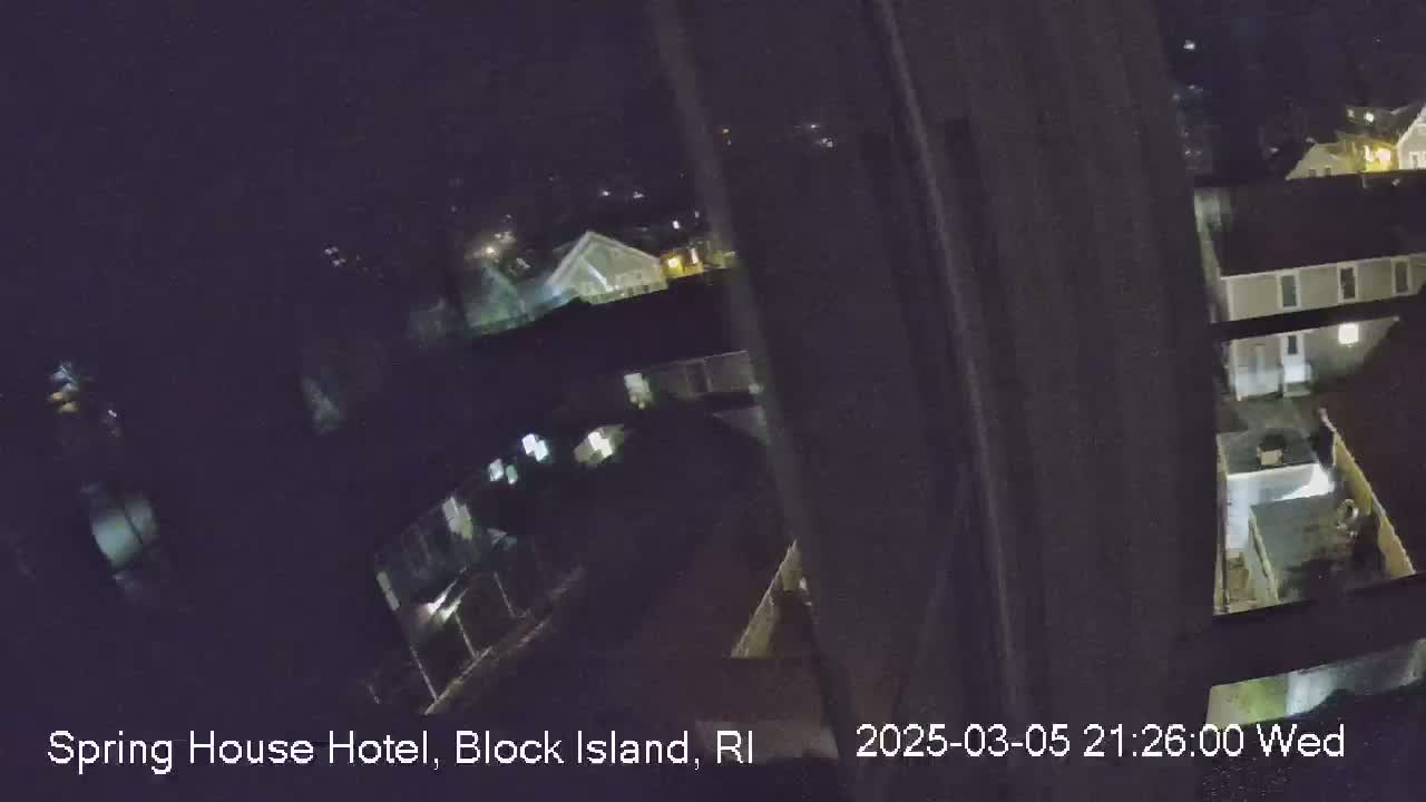 A nighttime view from a window shows several buildings and a courtyard, under dark, clear skies.