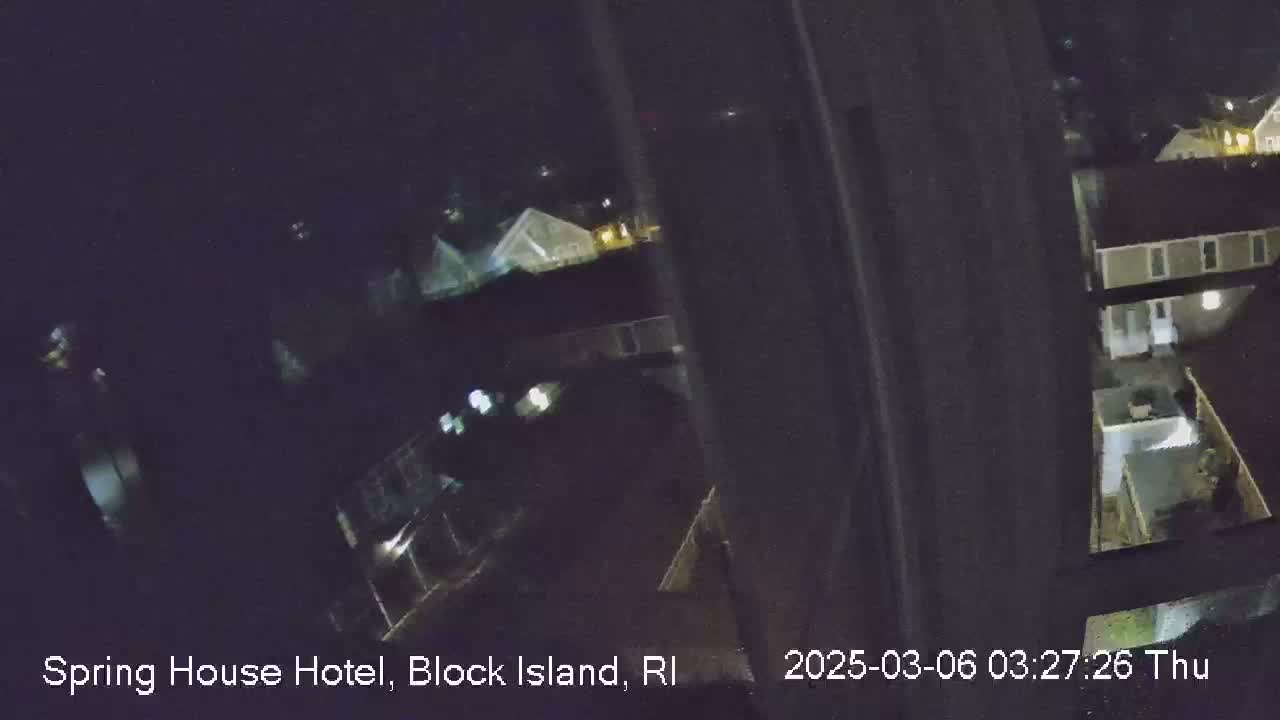 A nighttime, low-light view from a window shows several buildings and a yard.