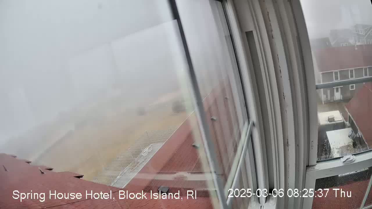 A foggy view of a red-roofed building and surrounding area is seen from inside through a window.