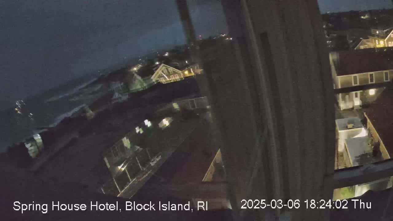 A nighttime, slightly overcast view from a window shows a dark ocean, and a collection of dark buildings with a few lights on.