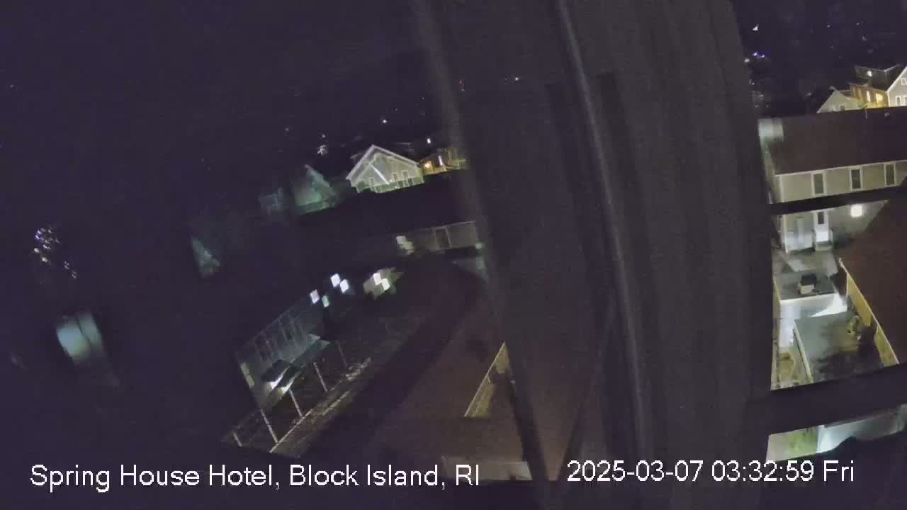 A nighttime, high-angle view from inside a building shows several houses and yards in the darkness.