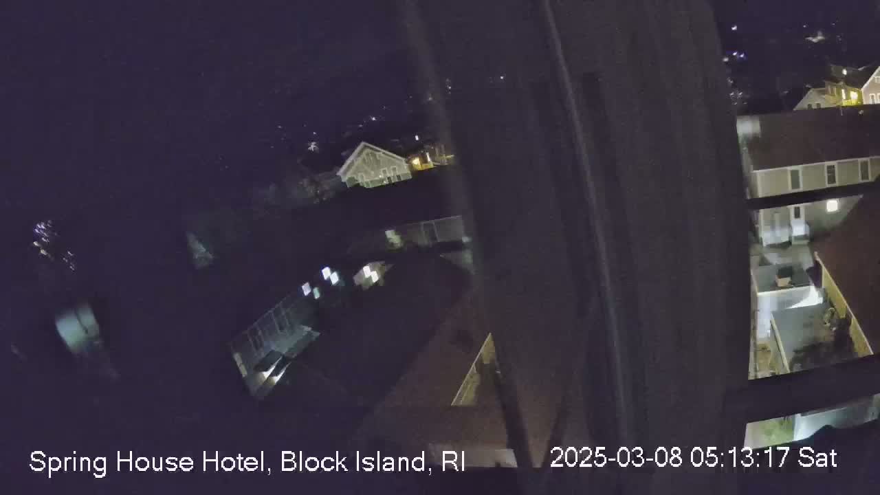 A nighttime, high-angle view from inside a building shows several other buildings and yards below.