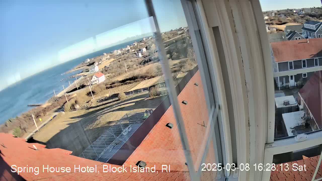 A high-angle view from a window shows a calm ocean, coastal buildings, and a clear sunny day.