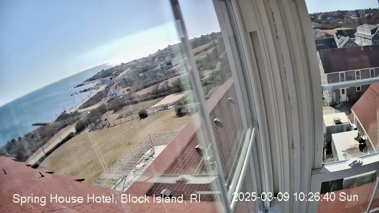 A sunny view from a window shows a coastal town, ocean, and buildings, with some land appearing barren.