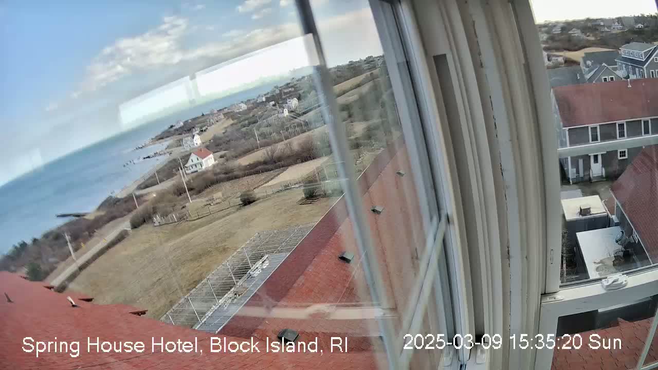 A view from a window shows a partly sunny day overlooking a coastline, houses, and open land.