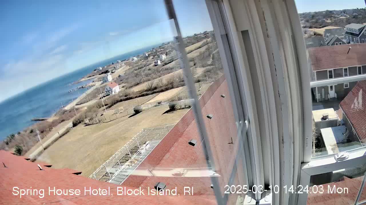 A view from a window shows a coastal town on a sunny day, with a body of water and buildings visible in the distance.