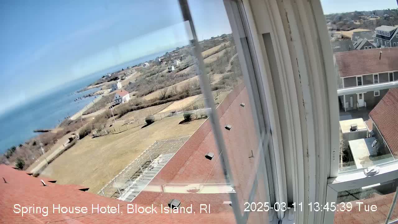 A high-angle view from a window shows a coastal landscape on a sunny day, with buildings, a shoreline, and ocean visible.