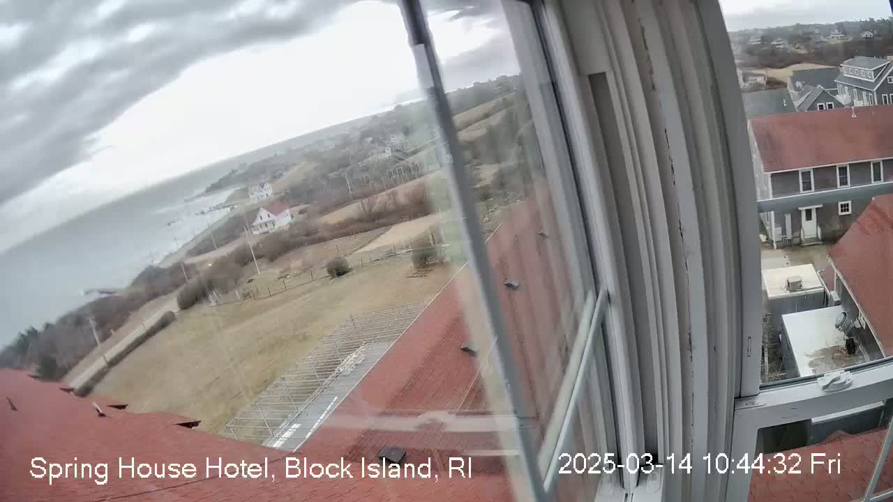 A view from a window shows an overcast day overlooking a coastal town with houses and a body of water, seen from what appears to be a hotel.