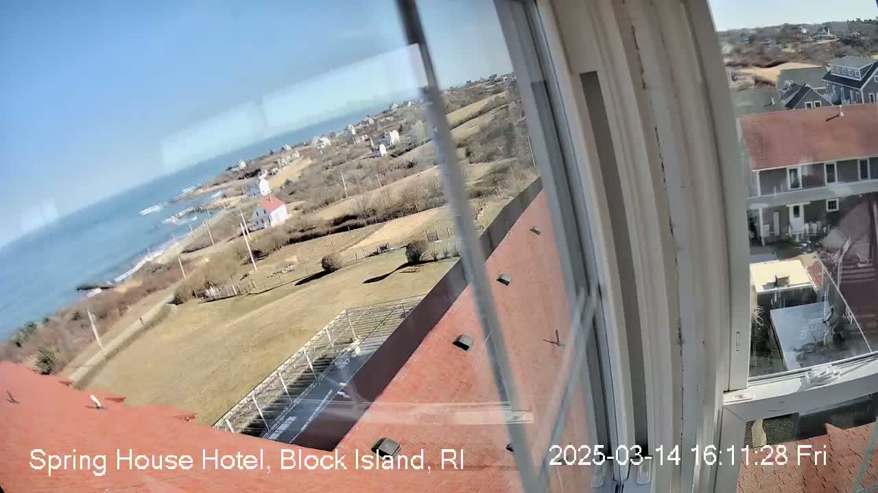 A view from a window shows a coastal scene on a sunny day, with ocean, houses, and grassy areas visible.
