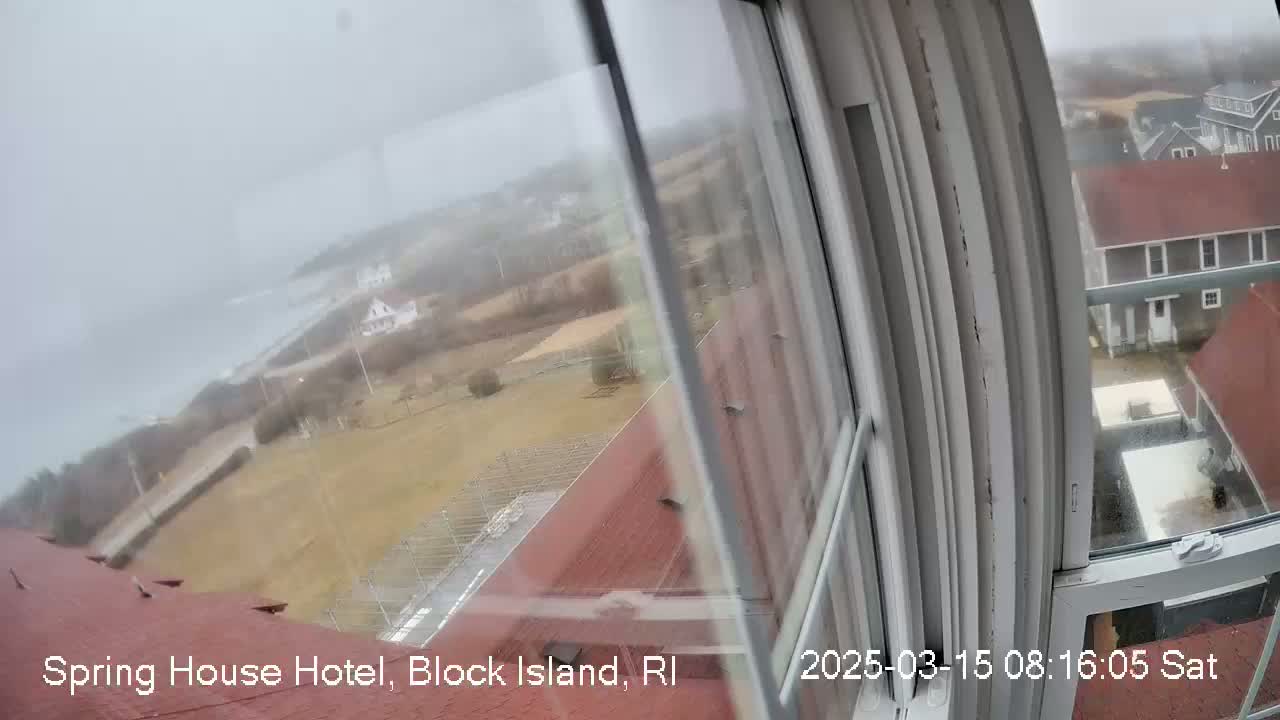 A foggy view from a window shows a coastal landscape with buildings and a body of water in the distance.