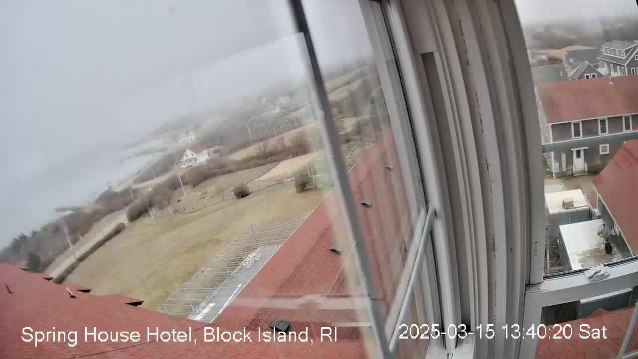 A foggy, overcast view from a window shows a coastal scene with buildings, a body of water, and a section of grassy land.