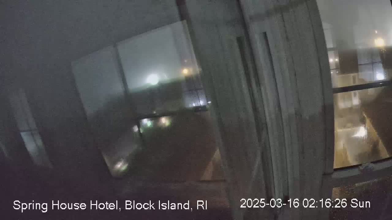 A nighttime view through a rain-streaked window shows blurry, dimly lit buildings and streetlights.