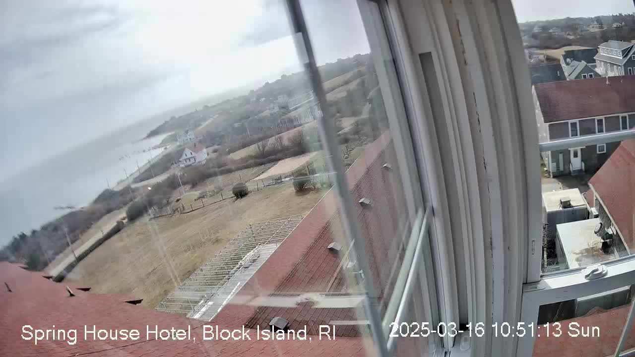 A slightly overcast view from a window shows a coastal town, ocean, and a building's red roof.