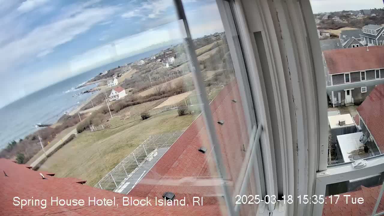 A mostly sunny view from a window shows a coastal scene with houses, a road, and ocean in the distance.