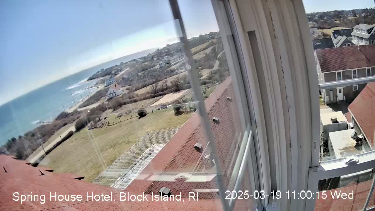A sunny view from a window shows a coastal scene with a body of water, buildings, and grassy areas.
