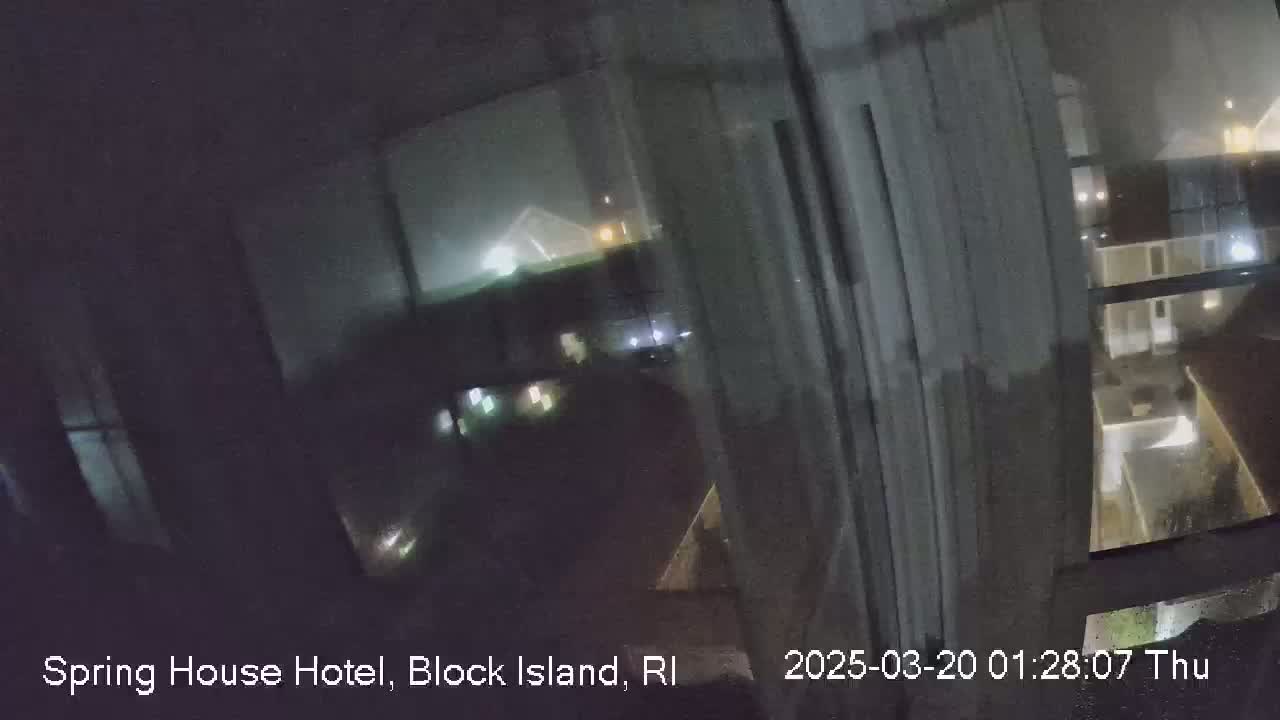 A nighttime view through a rain-streaked window shows dimly lit buildings and a parking lot.