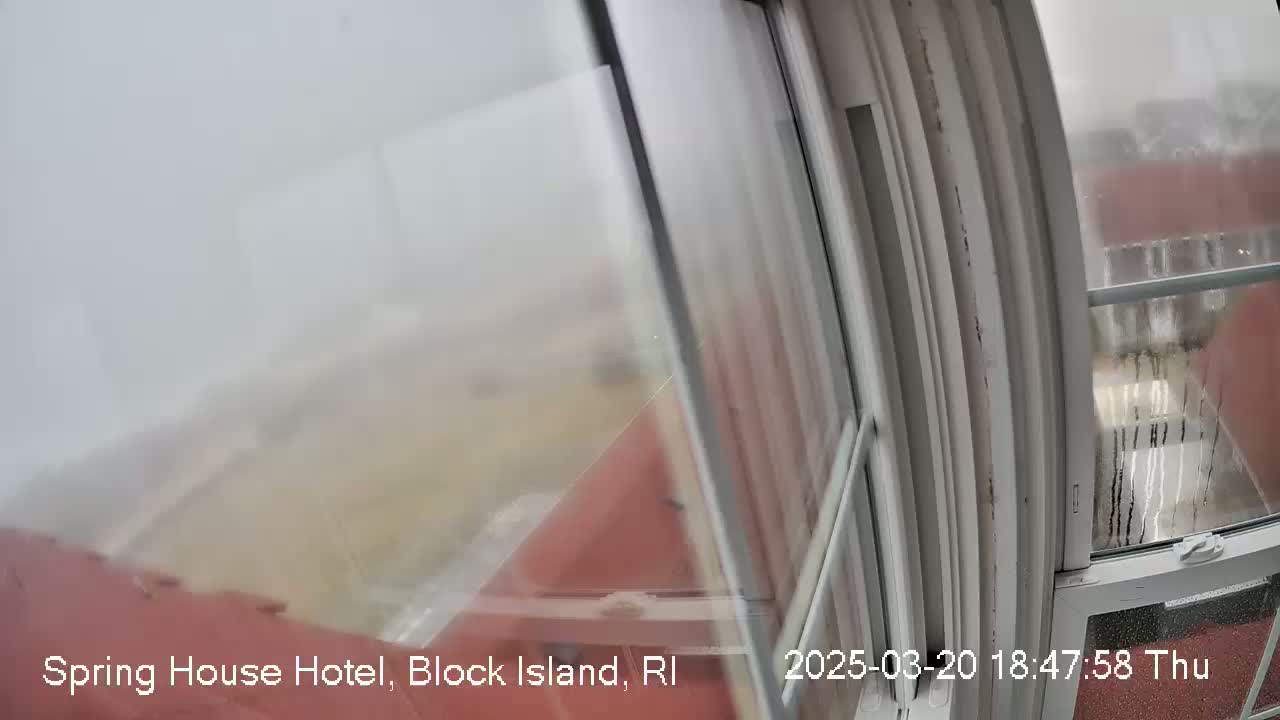 A hazy, rainy view is seen from a window, showing a blurry reddish-brown building and landscape beyond.