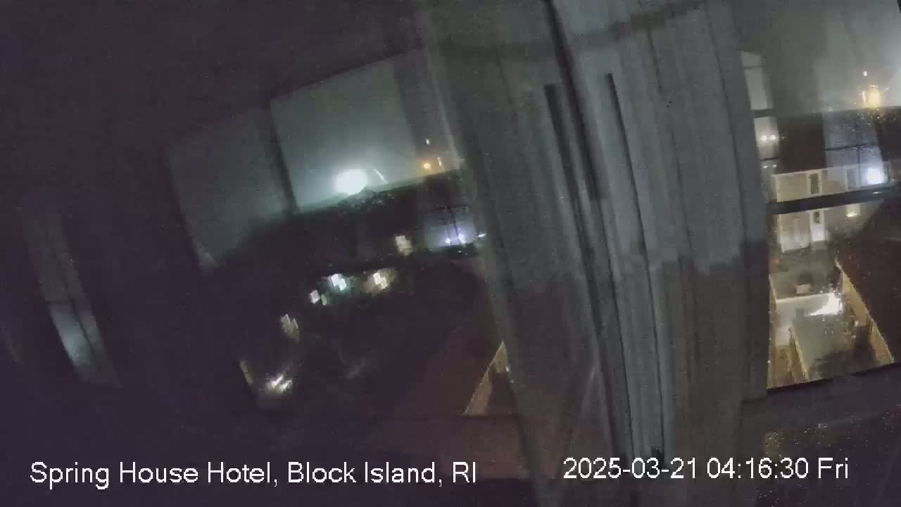 A nighttime view from a window shows a stormy scene with lightning in the distance and rain on the glass.