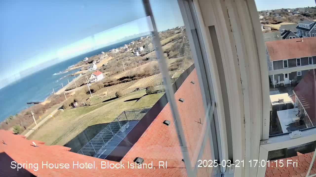 A view from a window shows a sunny coastal scene with a body of water, houses, and grassy areas.