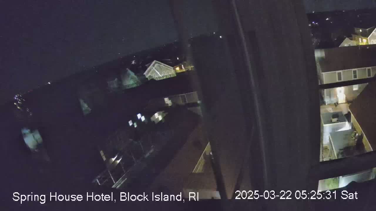 A nighttime, high-angle view from a window shows several houses with some lights on, partially obscured by the window frame.