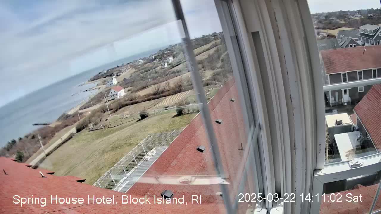 A view from a window shows a partly cloudy day overlooking a coastal area with houses, fields, and the ocean.