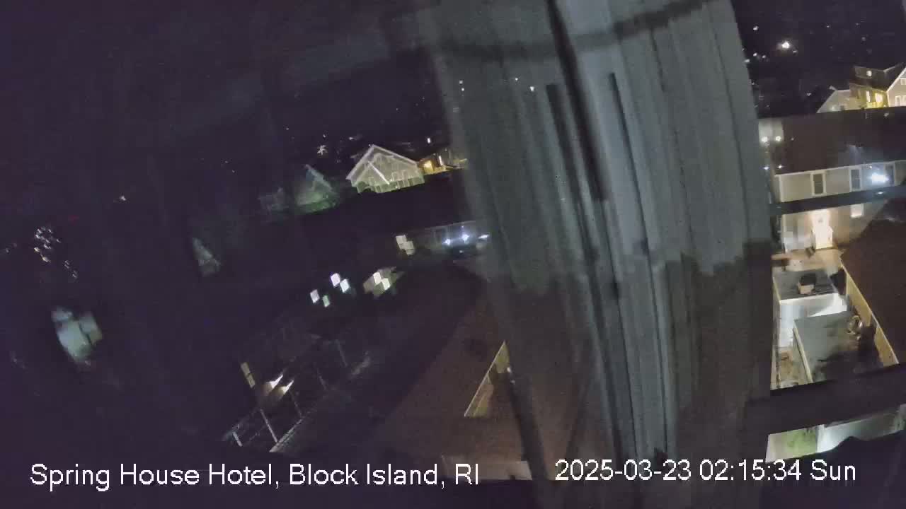 A nighttime, outdoor view from a window shows several buildings and a partially visible yard.