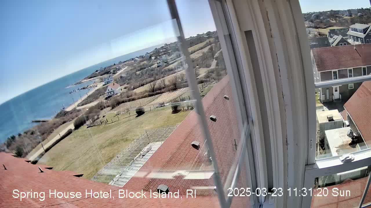A sunny view from a window shows a coastal landscape with houses, a body of water, and grassy areas.