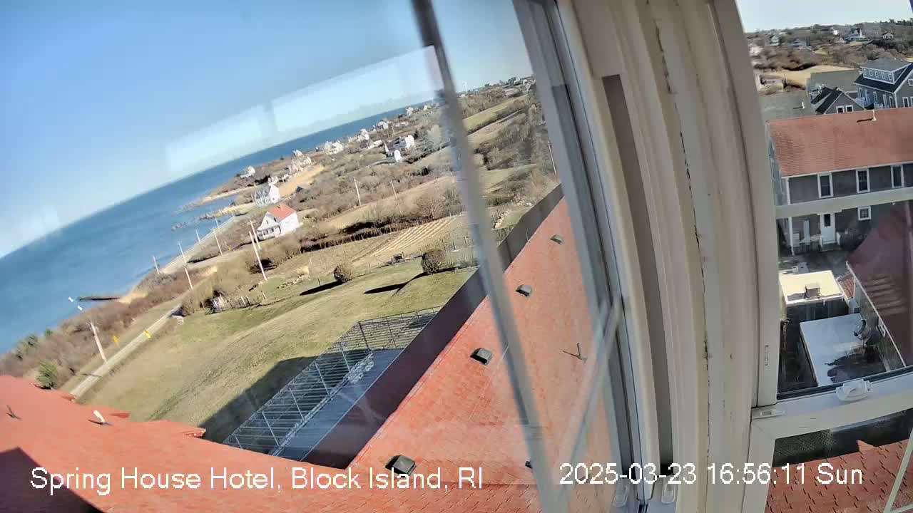 A sunny view from a window shows a coastal landscape with houses, a grassy area, and the ocean in the distance.