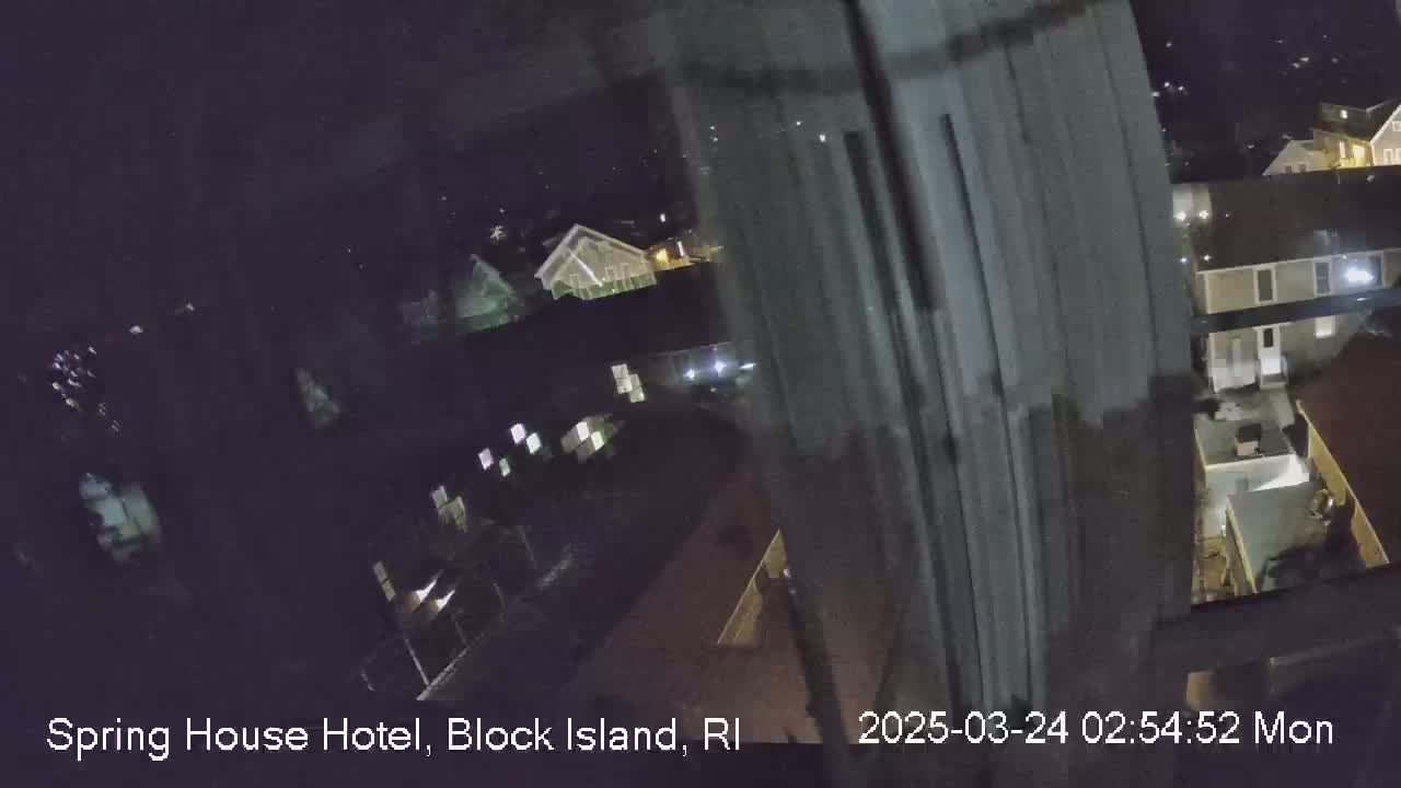 A nighttime, blurry view from a window shows dimly lit buildings and a parking lot.