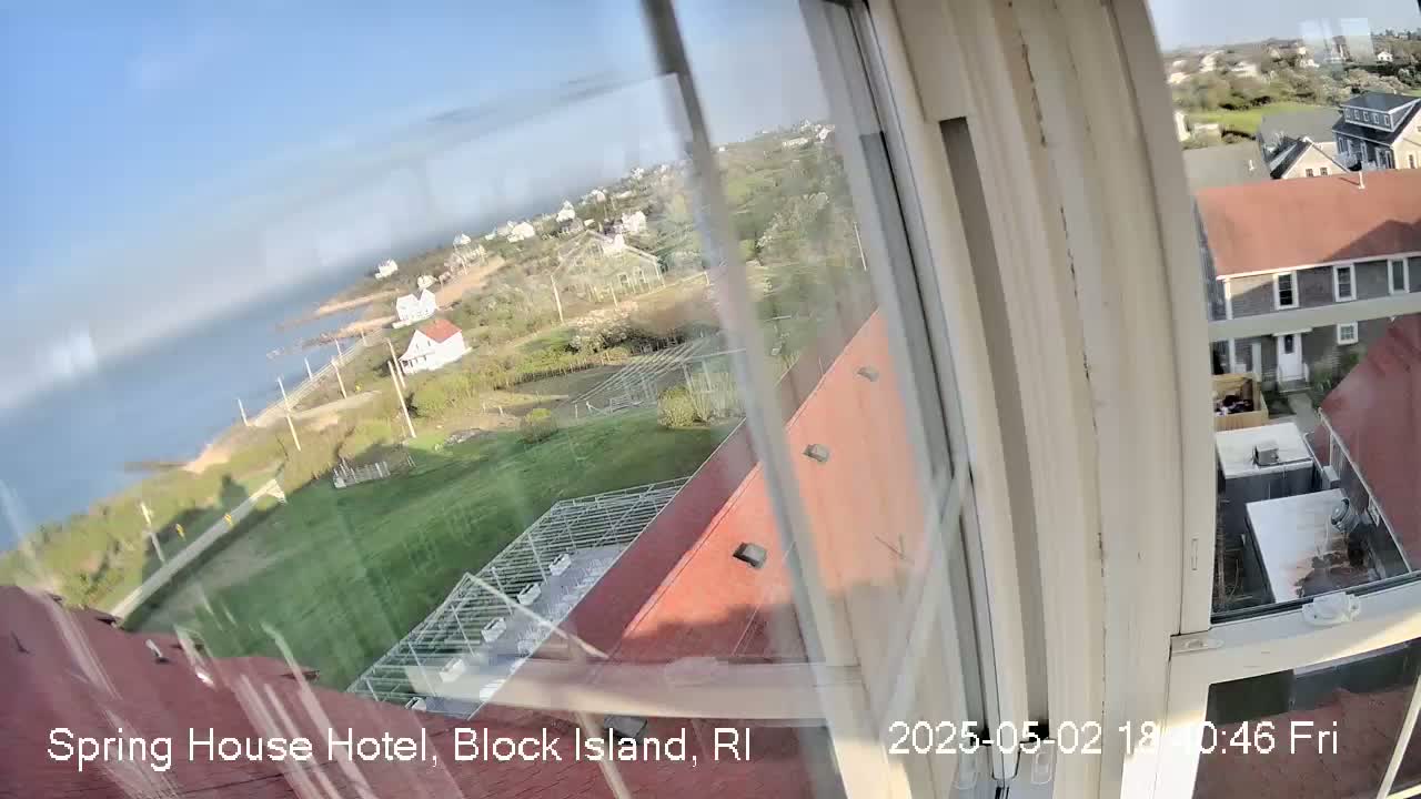 A view from a window shows a coastal area with houses, green lawns, and a body of water under a clear, sunny sky.