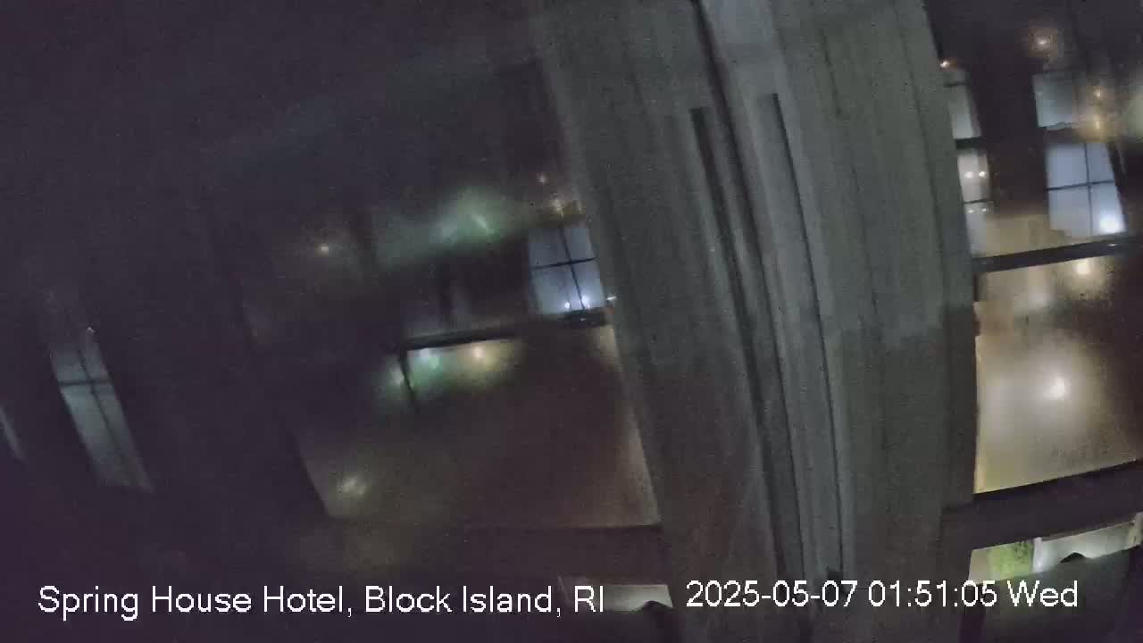 A nighttime view from a window shows dimly lit rooms and buildings beyond, possibly under rainy conditions.