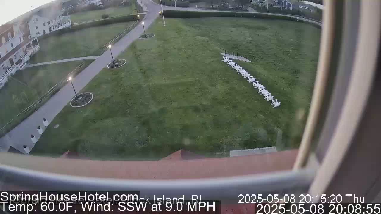 A high-angle view shows a grassy area with a row of white chairs, a building, and walkways, under partly cloudy skies with a southwest wind of 9 mph and a temperature of 60 degrees Fahrenheit.