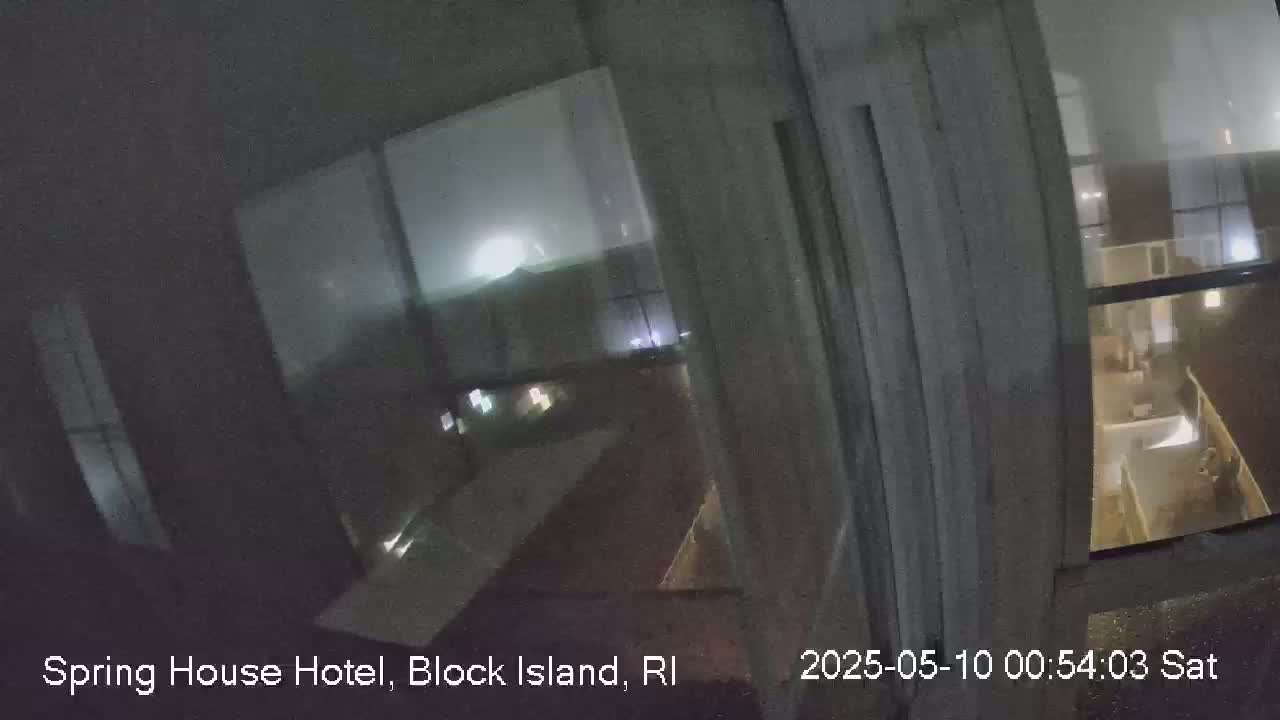 A nighttime view from inside a building shows a stormy scene outside through a window, with lightning visible in the distance.