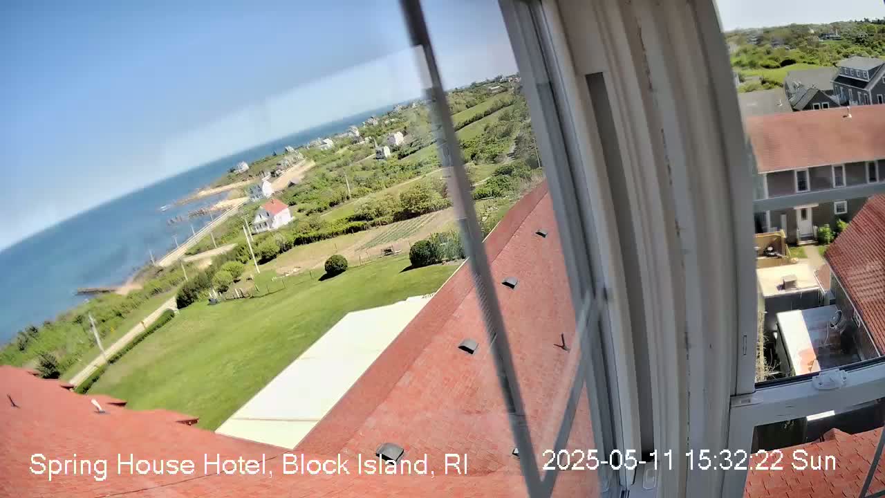 A sunny view from a window shows a red roof, green lawns, a body of water, and nearby buildings.