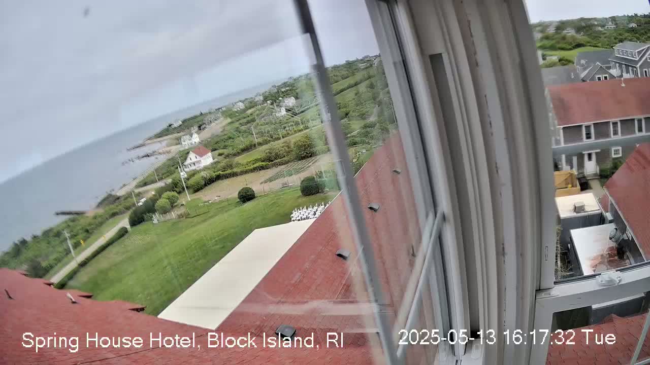 A view from a window shows a coastal scene with overcast skies, featuring a body of water, houses, and green lawns, all seen from an elevated position.