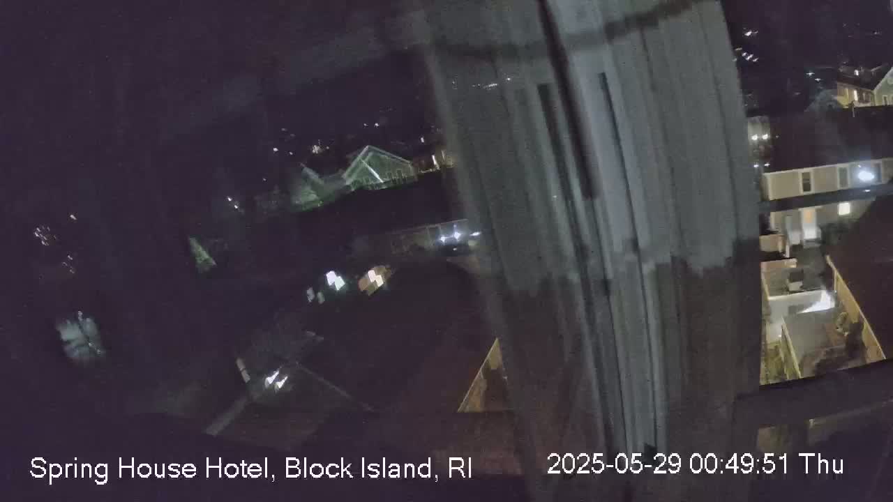 A nighttime, blurry view from a window shows several buildings and houses illuminated by lights.