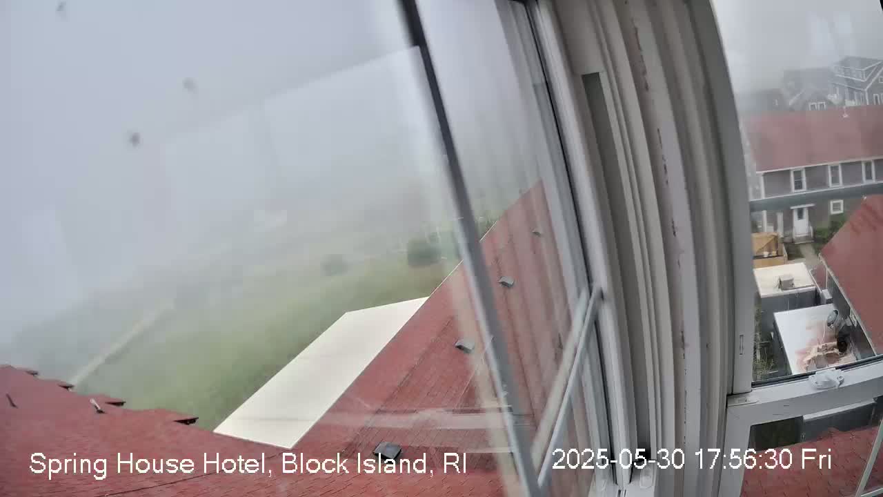 A foggy view from a window shows a red roof, a white awning, and other buildings in the distance.